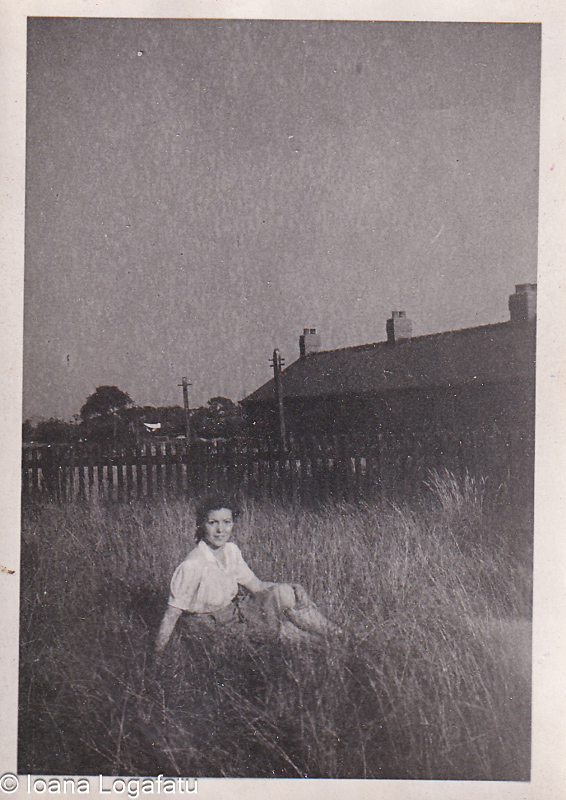 Young girl sitting in tall grass near homes
