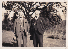 Two gentlemen stand proudly in a tranquil garden