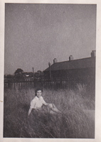 Young girl sitting in tall grass near homes