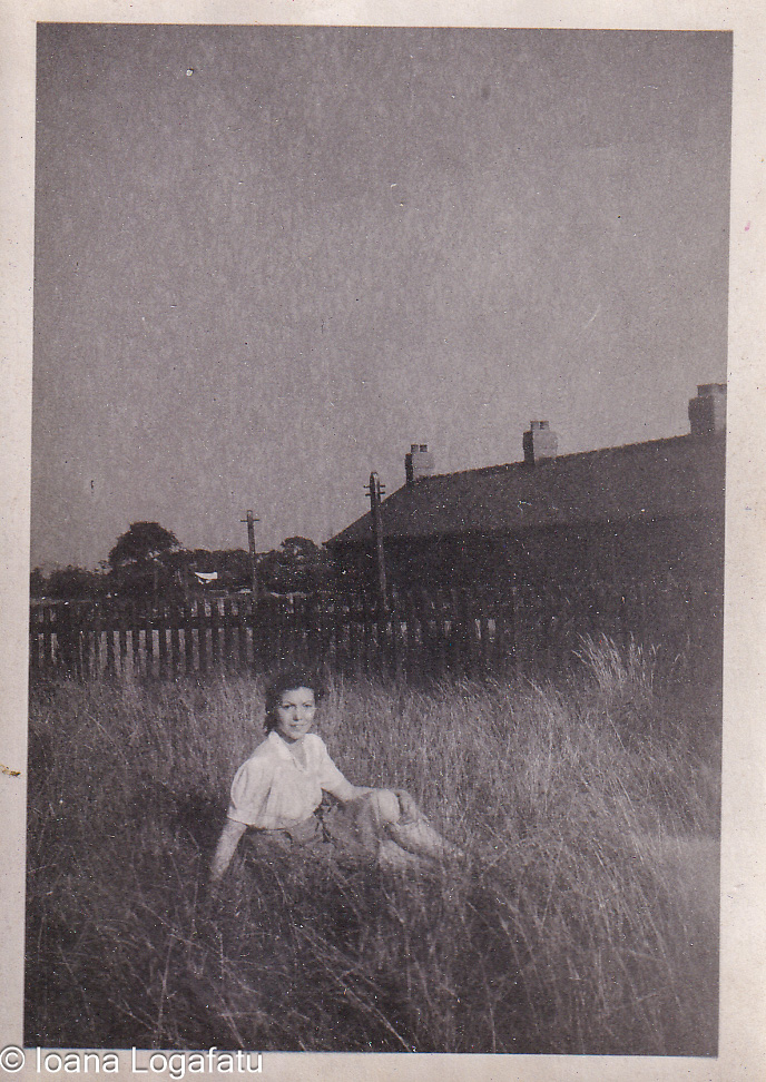 Young girl sitting in tall grass near homes