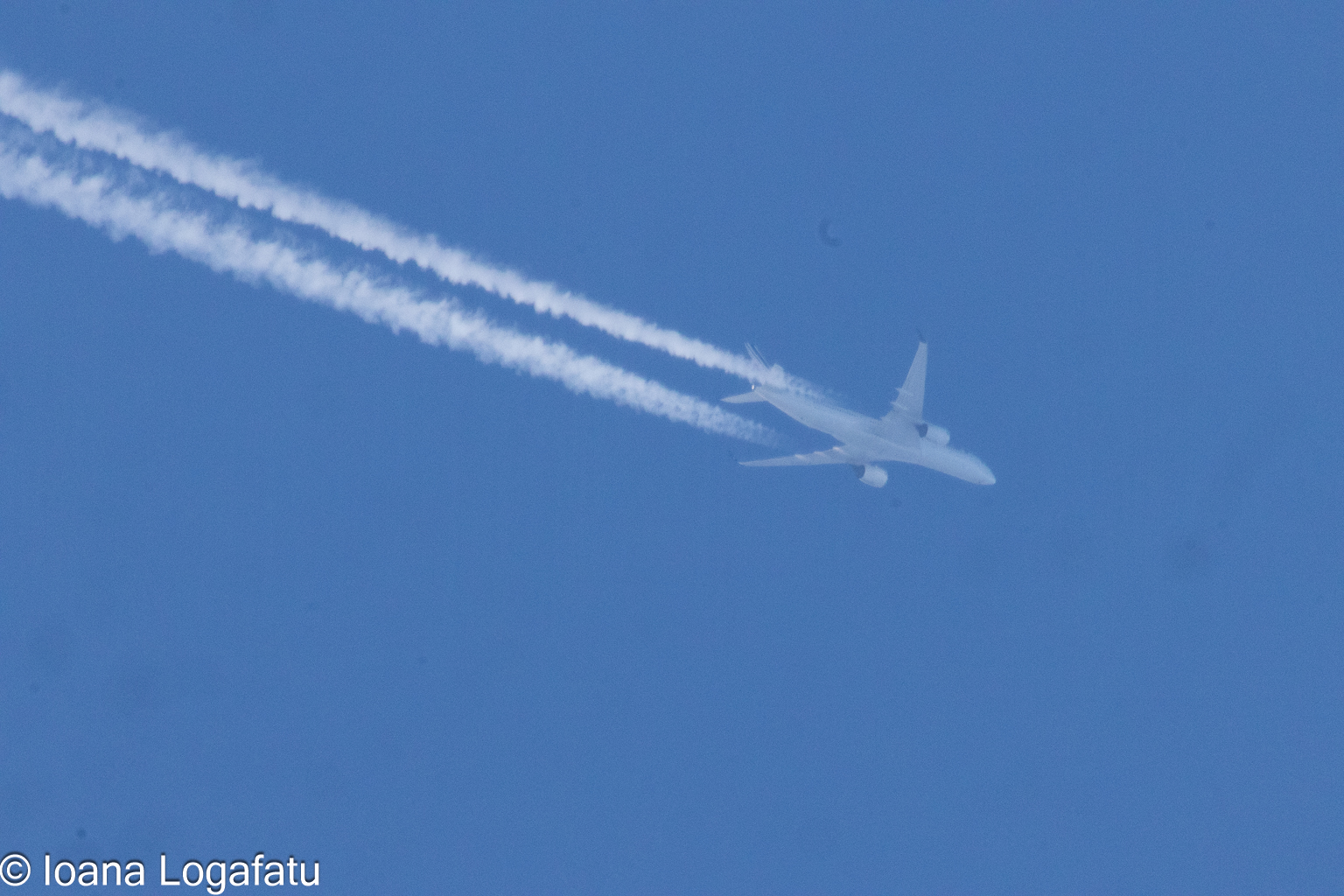 Jet soaring through clear blue sky with trails