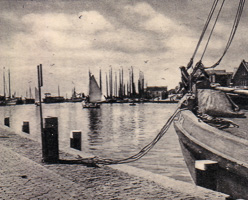 Boats docked near a calm harbor with sails up