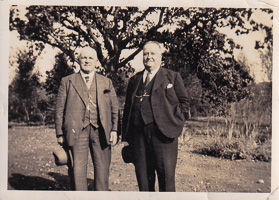 Two gentlemen stand proudly in a tranquil garden