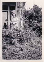 Woman standing amid lush greenery near a window