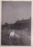 Young girl sitting in tall grass near homes