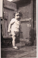Child standing by a wooden fence in a backyard